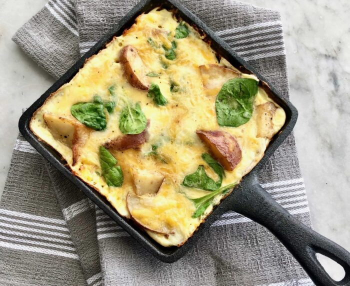 quiche with potatoes and spinach in a cast iron skillet.