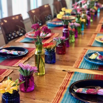 fiesta plates and colorful flowers on a long table with chairs