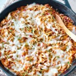 cheesy spaghetti in a black cast iron skillet with a wooden spoon.