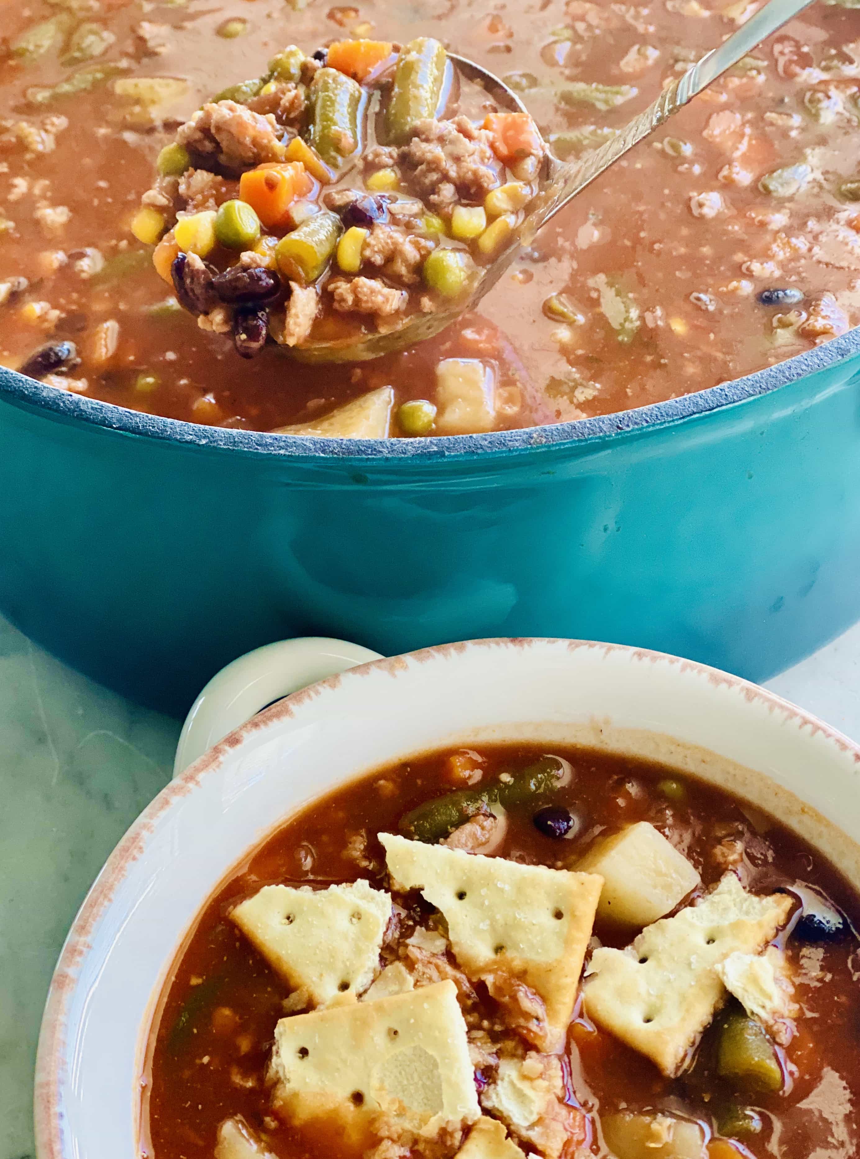 Vegetable Beef Soup in a blue dutch oven with a bowl of it and crackers on top