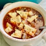 vegetable beef soup with crackers in a white bowl