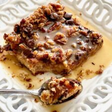 slice of chocolate bread pudding with pecans and caramel rum sauce on a white plate