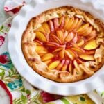 peaches arranged in a circle inside a crust on a white pie plate with peach jam