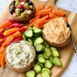 olives, pimento cheese and spinach artichoke dip with carrots, pepper and cucumbers on a wooden board