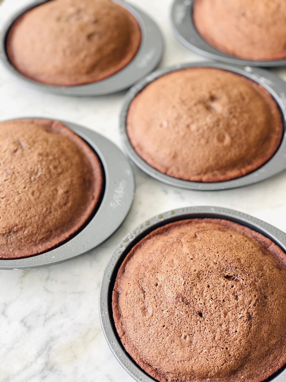 five cake pans filled with chocolate cake batter