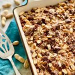 chocolate cake topped with peanuts, chocolate peanut butter cups in a white dish on a blue napkin