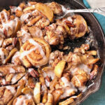 monkey bread apple cobbler in a cast iron skillet with a spoon taking a bite