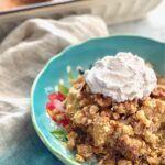 apple walnut dump cake in a blue bowl with a dollop of cinnamon whipped cream on top.
