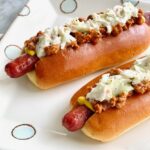 two hot dogs with creamy coleslaw and chili on top