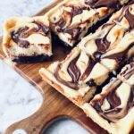 nutella cheesecake brownies with swirled nutella on a wooden board
