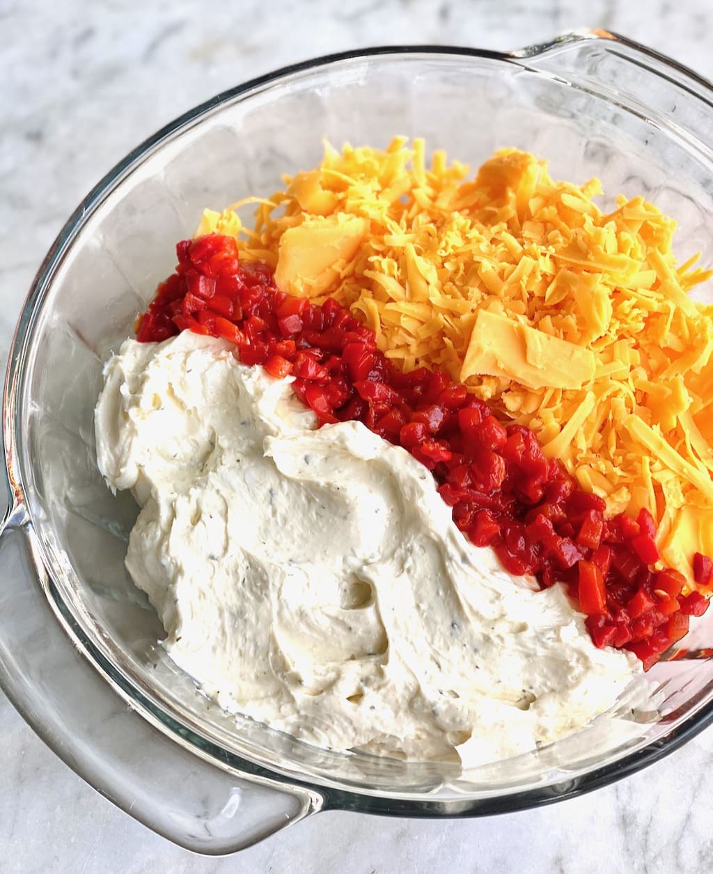 cream cheese, pimentos and shredded cheddar in a glass bowl.