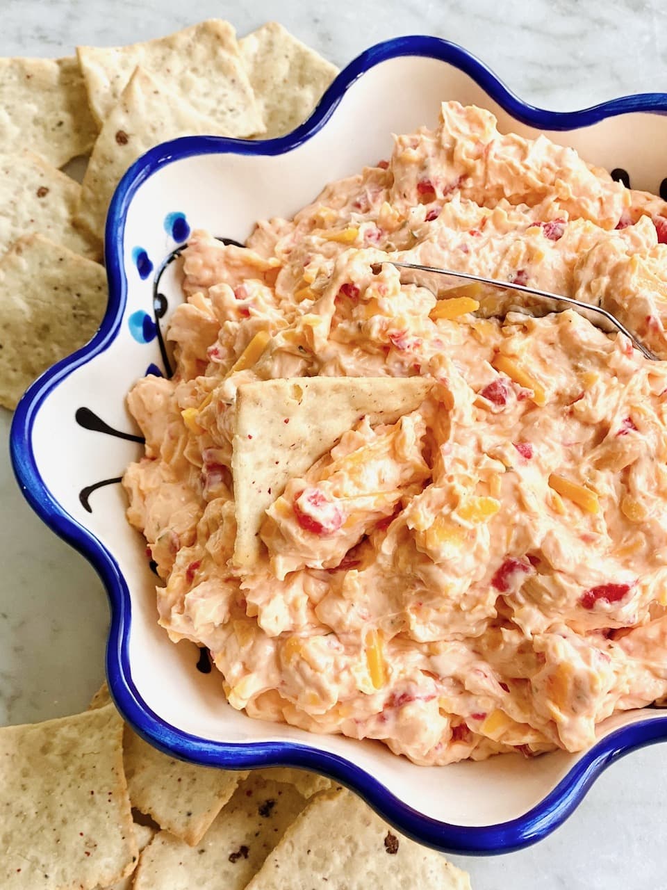 a bowl of pimento cheese with crackers on the side and one dipping in the bowl.