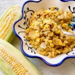 bowl of sweet corn casserole beside two ears of corn.