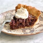slice of chocolate chip pecan pie on a floral plate with a fork.