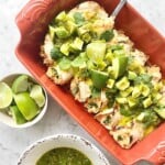 limes, cilantro, salsa verde and avocado top green burritos in an orange dish.