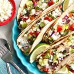 baja chicken tacos topped with pico de gallo and cojita cheese in a blue bowl with a fork and spoon.