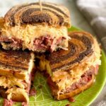 three corned beef reuben sandwiches stacked on a green plate.