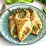 asparagus bundles wrapped in puff pastry on a teal plate.