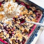 spoon lifting a bite of blueberry crumble out of a blue dish.