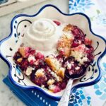 southern blackberry cobbler in a bowl with a big scoop of vanilla bean ice cream.