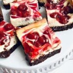 up close photo of cherry cheesecake brownie bars on a white cake plate.