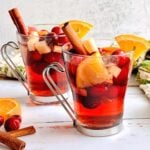 two clear glasses filled with mulled apple cider and oranges, apples and cranberries.