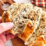 hand pulling cheese stuffed garlic bread apart on a wooden cutting board.