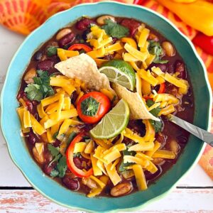 chili made in a dutch oven topped with cheese, chips, peppers and limes.
