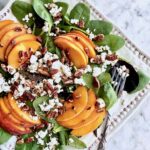 fresh peach salad topped with goat cheese and toasted pecans on a bed of spinach.