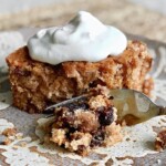 fork taking a bite from a slice of prune cake with whipped cream on top.