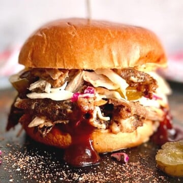 dutch oven pulled pork sandwich with slaw and bbq sauce dripping onto plate.