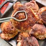 smoked chicken thighs being held up by kitchen tongs.