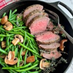 beef tenderloin and green beans in a black cast iron skillet.