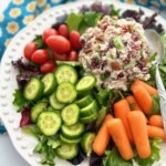 A scoop of cranberry pecan chicken salad on a bed of lettuce with fresh vegetables.