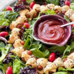 pigs in a blanket wreath surrounded by mixed greens and tomatoes.