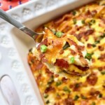Twice baked mashed potatoes in a casserole dish being held up by a spoon.