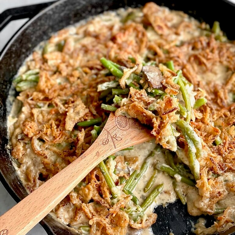 Green bean casserole without mushroom soup being lifted out of a cast iron skillet by a wooden spoon.