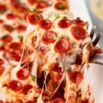 Spoon lifting up pizza bake in casserole dish.