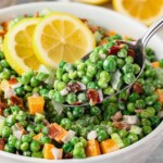 Green Pea Salad being lifted out of a white bowl with lemon slices on the side.