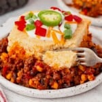 Cowboy Cornbread Casserole on a plate being sliced with a fork.