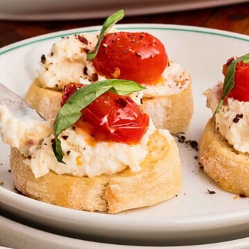Ricotta Cheese Dip being spread on a crostini topped with tomatoes and basil.