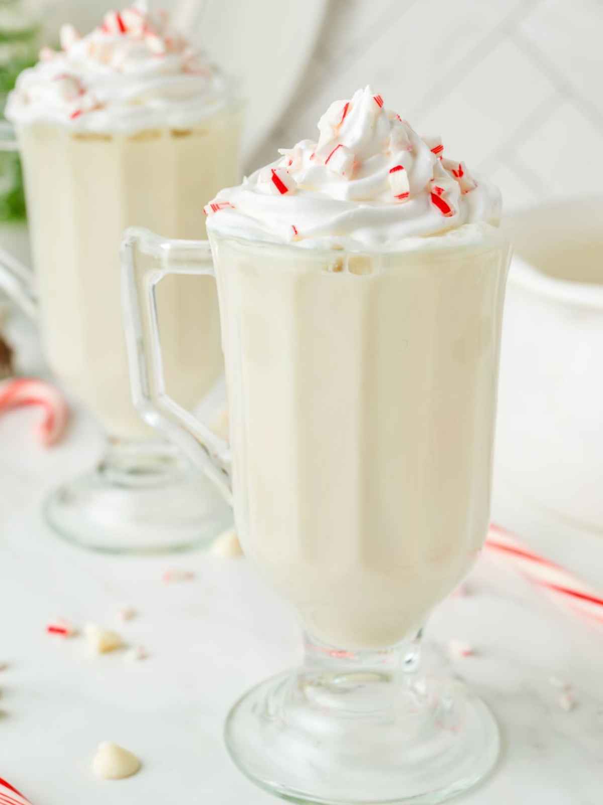 Mugs of peppermint white hot chocolate with whipped cream and candy cane garnish.