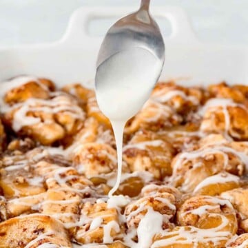 Spoon drizzling icing over a baking dish filled with apple pie cinnamon rolls.