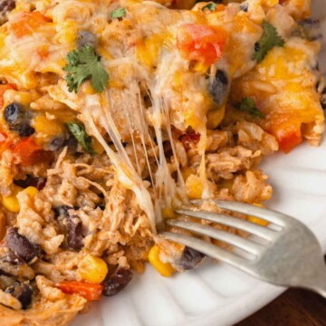 Fork pulling cheese off the top of chicken and rice casserole.