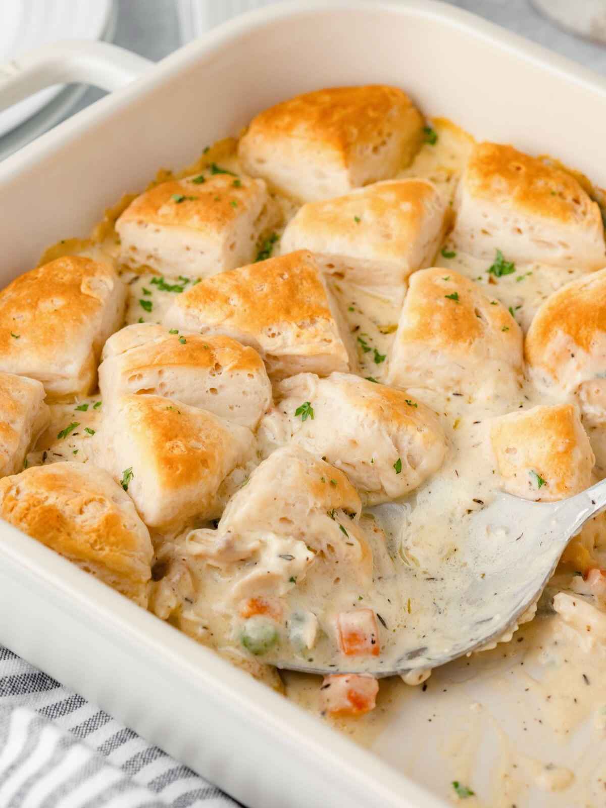 Large spoon dishing out chicken casserole from baking dish.
