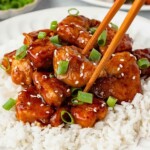 Honey sesame chicken being picked up by chopsticks.