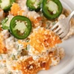 A fork holds a cheesy, creamy Jalapeño Popper Chicken Casserole bite topped with sliced jalapeños on a white plate.