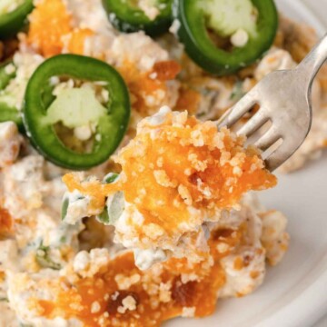 A fork holds a cheesy, creamy casserole bite topped with sliced jalapeños on a white plate—a classic comfort dish from Quiche My Grits.
