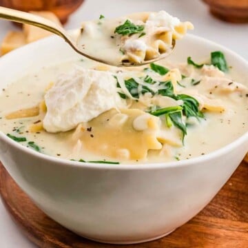 White chicken lasagna soup being held up by a spoon.