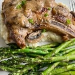 Pork chop on mashed potatoes and a side of asparagus.